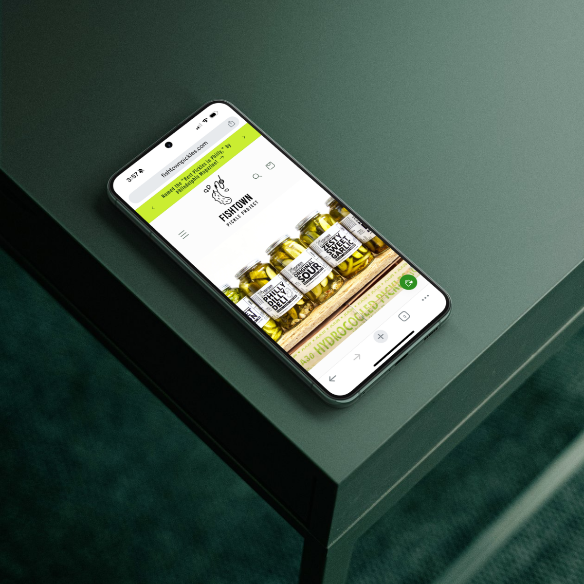 A smartphone on a green table showcasing a mobile-optimized ecommerce website for Fishtown Pickle Project, emphasizing responsive design and conversion-driven email growth strategies for small food and beverage businesses.