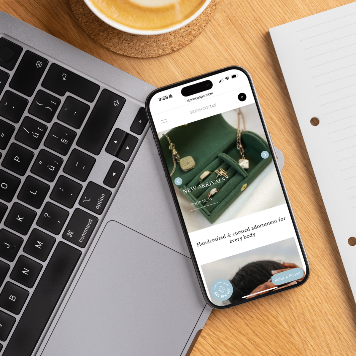 Mobile view of handcrafted jewelry ecommerce site displayed on iPhone, placed on a MacBook with coffee – example of responsive ecommerce website design by the team at Next Chapter Designs.